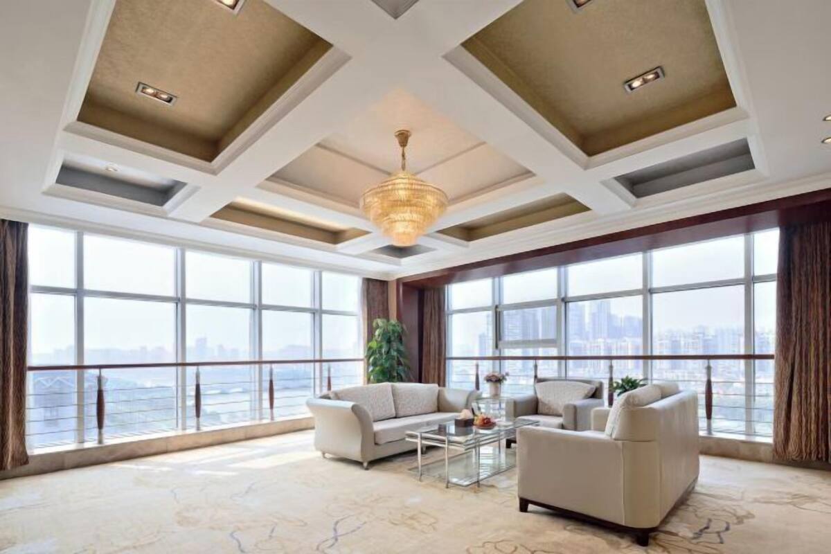 A spacious room with large windows, a chandelier, and a modern ceiling design.