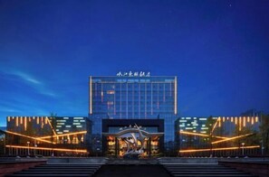 Un hotel moderno con una entrada destacada, un amplio frente de cristal y señalización iluminada.