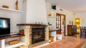 Een woonkamer met een open haard, een televisie en een eethoek met stoelen en een tafel.