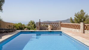 A clear blue swimming pool with a stone wall and a wooden fence, surrounded by greenery and a view of distant hills. - Cozy Holiday Home “La Monticana “ with Sea View, Wi-Fi, Air Conditioning, Pool & Terrace (Frigiliana)