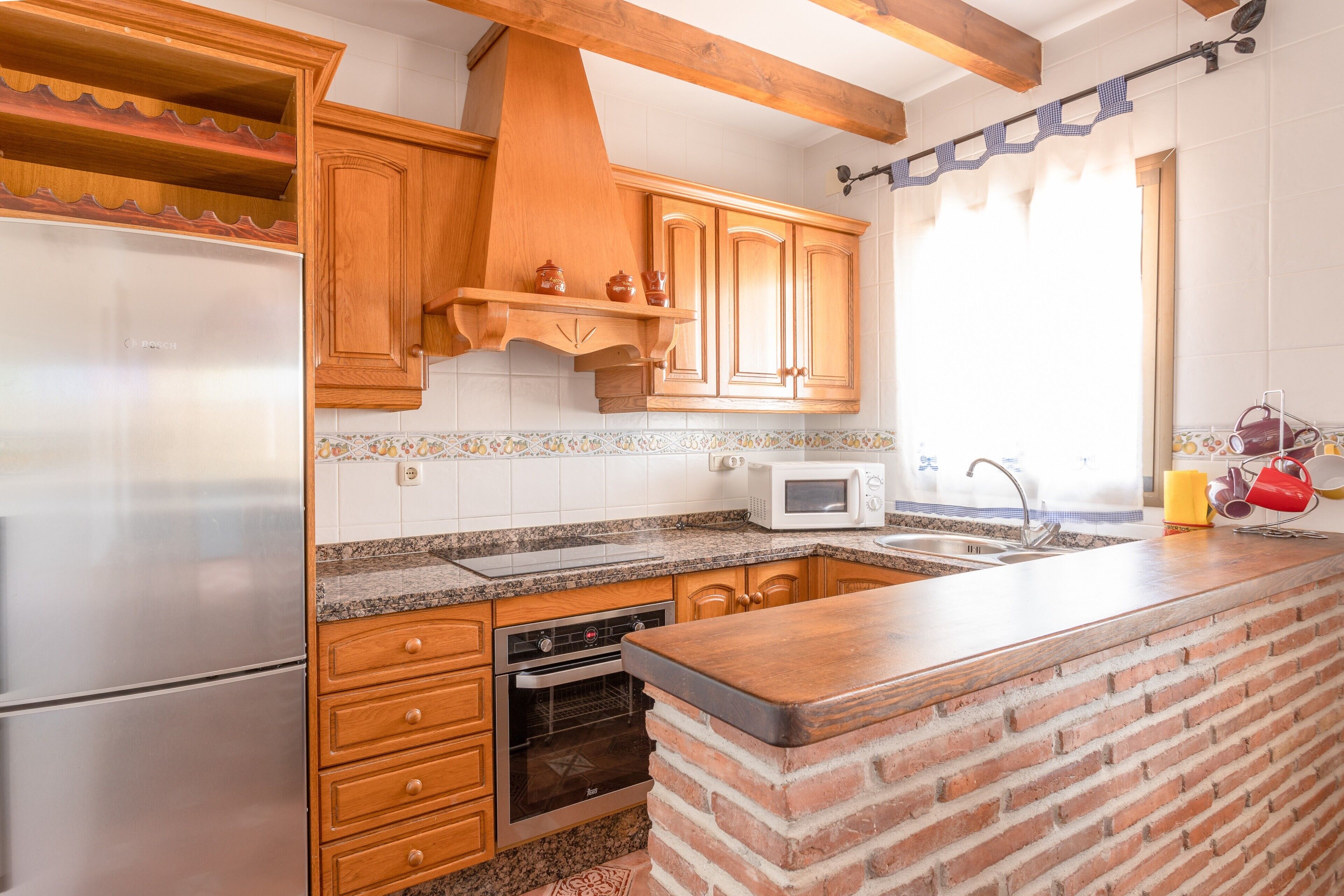 A kitchen with wooden cabinets, a brick island, a stainless steel refrigerator, and a microwave.