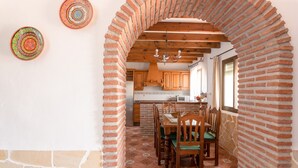 A dining area with a brick archway, wooden table, chairs, and a patterned floor. - Cozy Holiday Home “La Monticana “ with Sea View, Wi-Fi, Air Conditioning, Pool & Terrace (Frigiliana)
