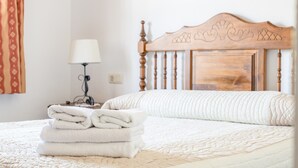 A neatly made bed with a white quilt, a wooden headboard, and a stack of white towels on the side. - Cozy Holiday Home “La Monticana “ with Sea View, Wi-Fi, Air Conditioning, Pool & Terrace (Frigiliana)