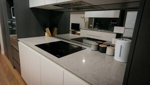 Une cuisine moderne avec des meubles blancs, une plaque de cuisson à induction noire et un four encastré. On y trouve également des planches à découper en bois et une machine à café sur le plan de travail.