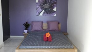 Een slaapkamer met een bed, paarse muren, een bloemschilderij en een kamerplant.