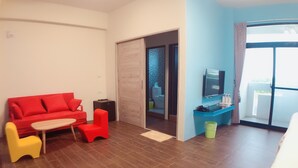 A hotel room with a red sofa, yellow chair, wooden table, and a TV on a blue stand.