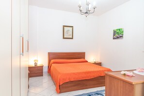 Une chambre à coucher avec un lit en bois, des tables de chevet avec des lampes, un lustre et des tableaux encadrés accrochés aux murs.