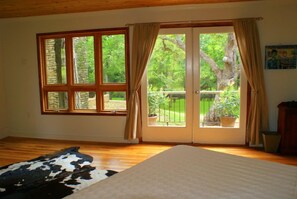 A room with a large window, a sliding glass door leading to a balcony, a wooden floor, and a cowhide rug.