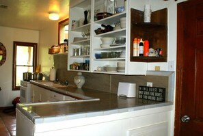 A kitchen with white cabinets, a countertop, and a sign on the wall. - Romantic country cottage right on the Cypress Creek! (Wimberley)