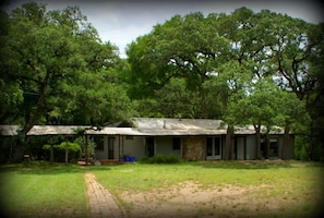 A rustic house with a stone foundation and metal roof, surrounded by lush greenery and trees.