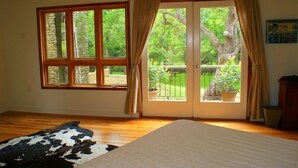 Una habitación con un ventanal grande, una puerta corrediza de vidrio que da a un balcón, piso de madera y un tapiz de cuero de vaca.