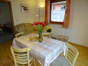 A dining area with a table set for two, a vase with flowers, and a window with curtains. - Vacation apartment 2 - Kos - Holiday home Ohm (Koserow)