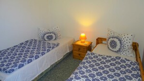 A bedroom with two single beds, each with a patterned bedspread and matching pillows. There is a nightstand with a lamp between the beds, and a framed picture on the wall above the beds. - Vacation apartment 2 - Kos - Holiday home Ohm (Koserow)