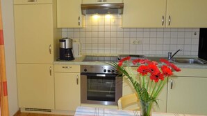 A kitchen with light yellow cabinets, a stainless steel oven, a coffee maker, and a vase with red flowers on the table. - Vacation apartment 2 - Kos - Holiday home Ohm (Koserow)