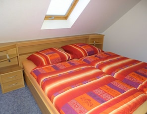 A bedroom with a skylight, wooden headboard, two bedside tables, and a bed with patterned bedding.