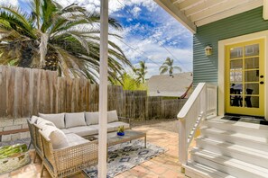 A patio with a white sofa, wicker chair, and a small table with a plant.