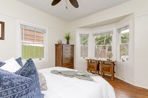 A bedroom with a bed, a dresser, a nightstand, and a window with a view of palm trees.