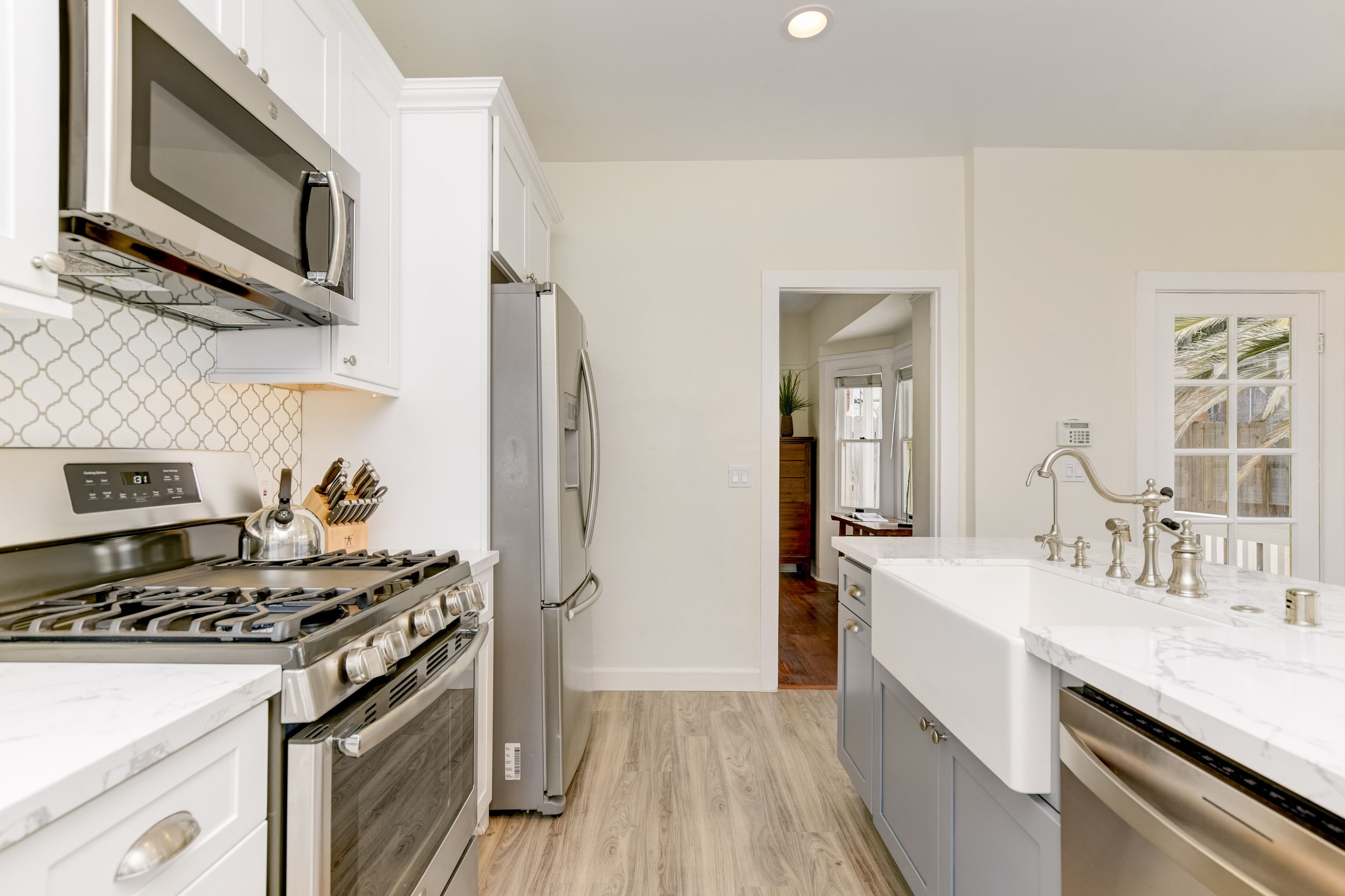 Une cuisine moderne avec des meubles blancs, des appareils électroménagers en acier inoxydable et un plancher en bois.