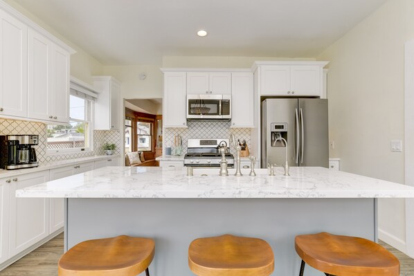 A modern kitchen with white cabinets, a marble island, stainless steel appliances, and three wooden bar stools.