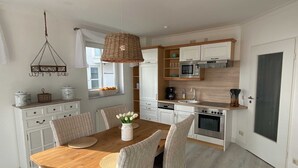 Une cuisine moderne avec des meubles blancs, une table à manger en bois, des chaises en osier et un luminaire suspendu.