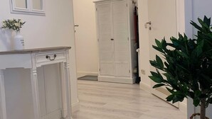 Un couloir avec une console blanche, un tapis rond en fibres tressées, une grande plante en pot et une armoire blanche.