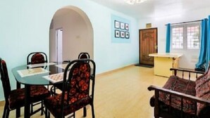 A dining area with a table and chairs, a sofa, a wooden cabinet, and a door leading to another room. - Wonder Hill Residency (Ootacamund)