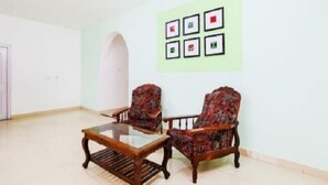 A room with two armchairs and a glass-top table. There is a wall with six framed pictures. - Wonder Hill Residency (Ootacamund)