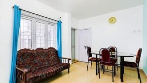A room with a sofa, dining table, chairs, and a clock on the wall. - Wonder Hill Residency (Ootacamund)