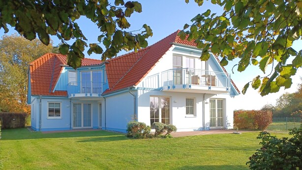 A two-story house with a red-tiled roof, large windows, and a well-maintained lawn. - An den Boddenwiesen III (Wustrow)