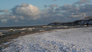 A beach with snow-covered sand, waves, and a person walking. - An den Boddenwiesen III (Wustrow)