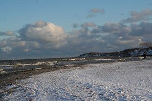 Ein Strand mit verschneitem Sand, Wellen und einer Person, die spazieren geht.
