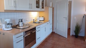 A modern kitchen with white cabinets, a built-in oven, a coffee maker, and a sink. - An den Boddenwiesen III (Wustrow)