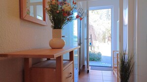 A hallway with a wooden console table, a vase with flowers, a mirror, and a door leading outside. - An den Boddenwiesen III (Wustrow)