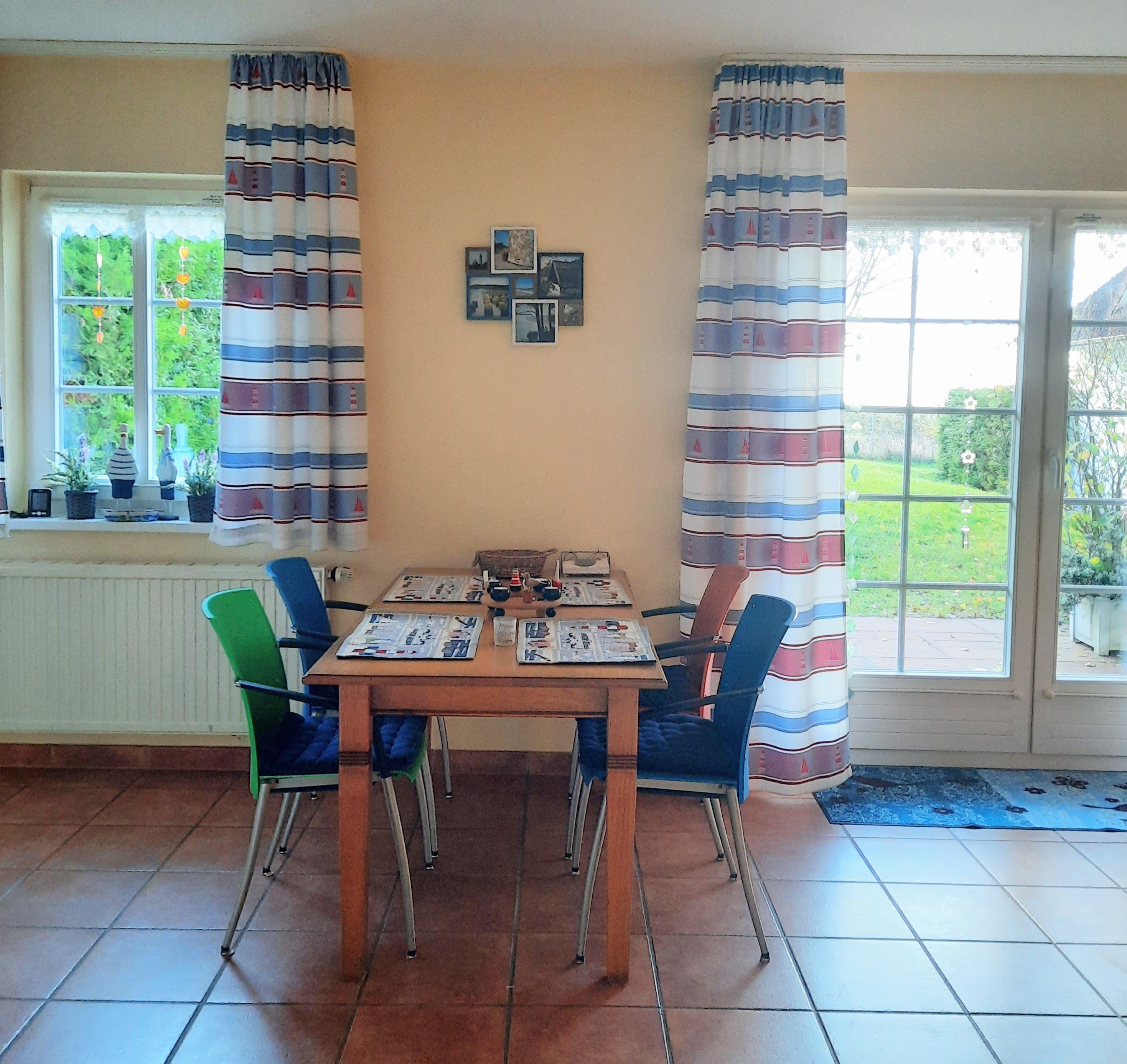 A dining area with a table set for four, surrounded by chairs, a window with curtains, and a view of greenery outside.
