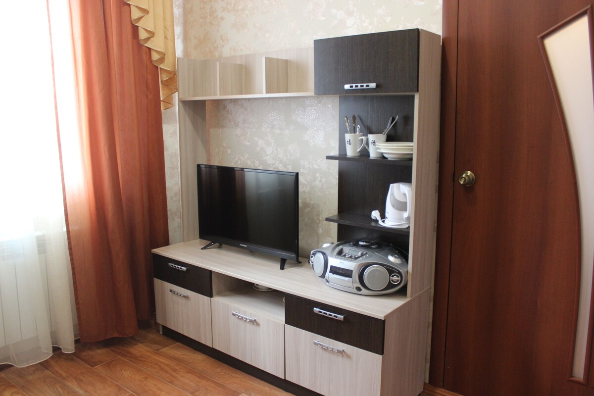 Un espacio habitable compacto con un televisor de pantalla plana, una cafetera y una radio sobre un mueble de madera.