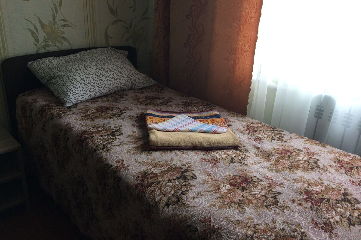 Una cama individual con una colcha floral, una almohada estampada y una manta doblada.