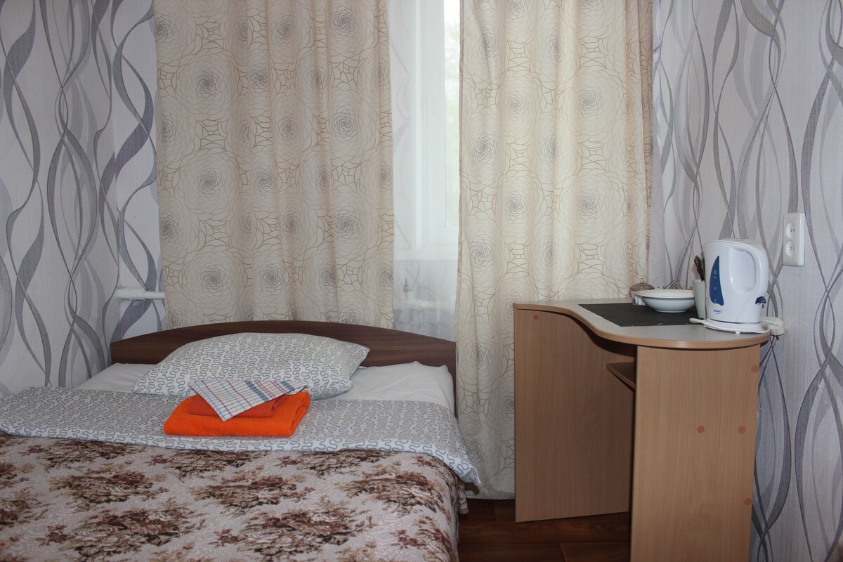 Un dormitorio con cama, escritorio, tetera y cortinas.