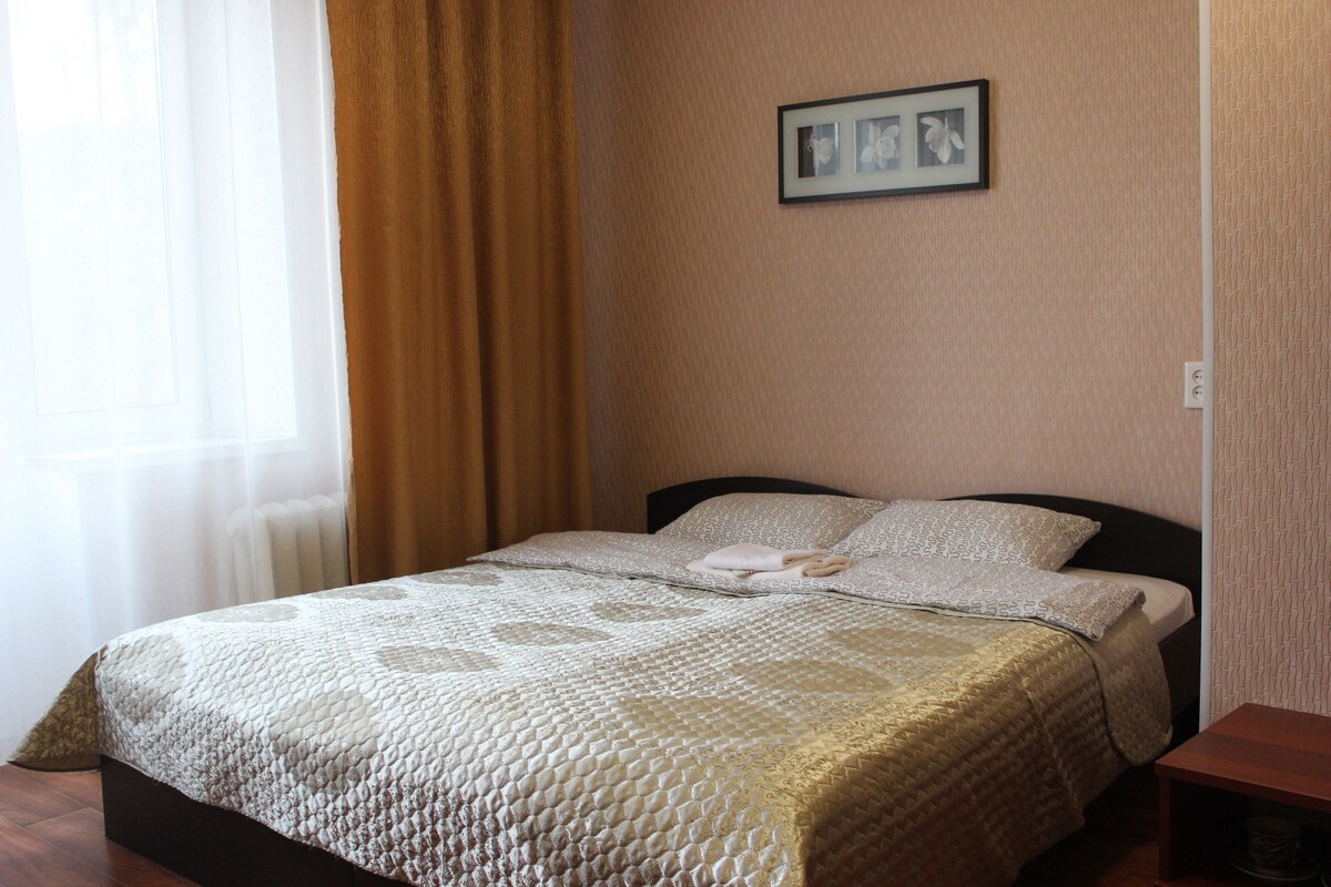 Una cama bien tendida con una colcha estampada, un cuadro en la pared y una mesita de noche de madera.