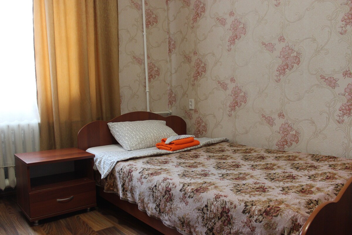 Un dormitorio con cama de madera, mesita de noche, radiador y papel tapiz floral.