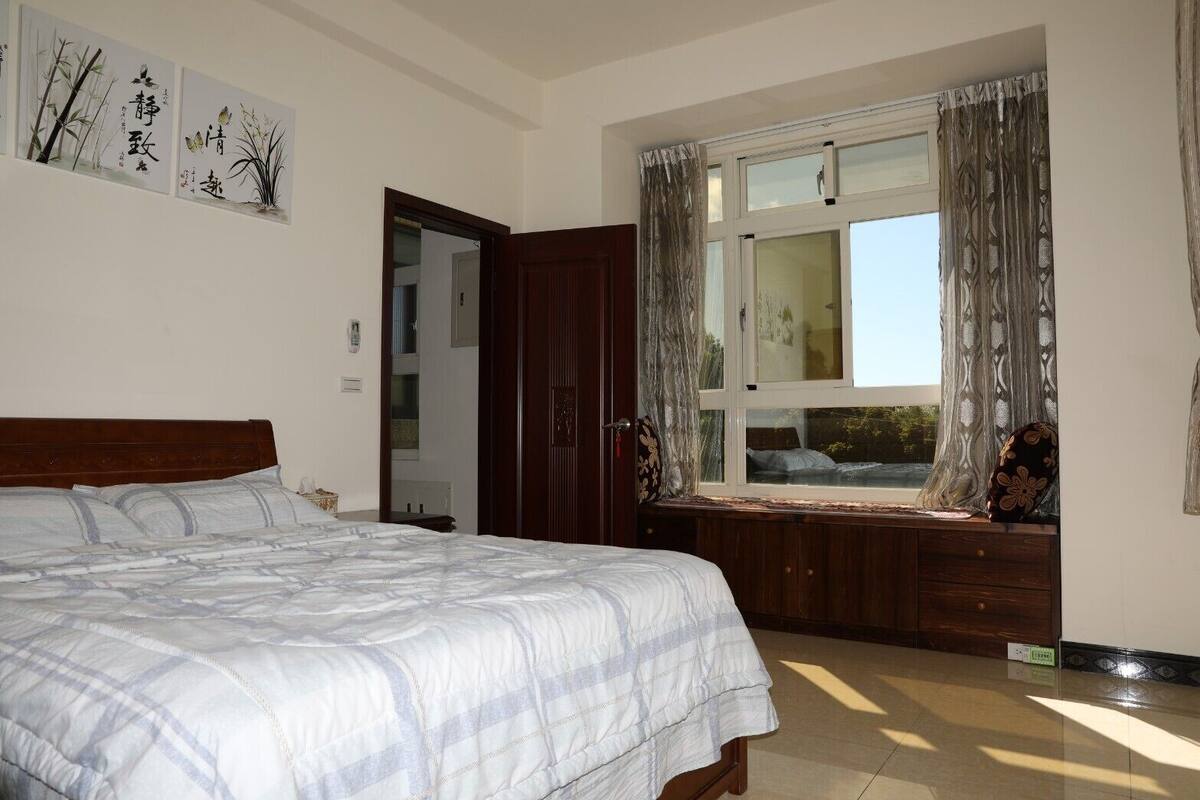 A bedroom with a large bed, a window with curtains, and artwork on the wall.