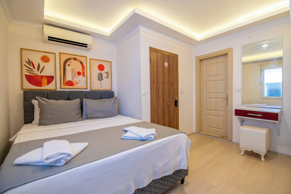 Habitación de hotel con cama, mesita de noche, espejo y una obra de arte en la pared.