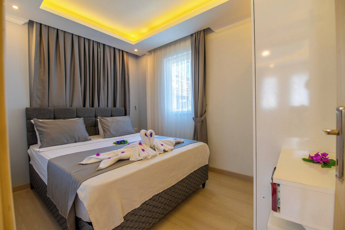 Una habitación de hotel con cama, cortinas, ventana, mesita de noche y espejo.