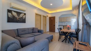 A modern living room with a grey sectional sofa, a dining area with a wooden table and chairs, and a kitchen visible through an open door. - Mykonut Apart Hotel (Fethiye)