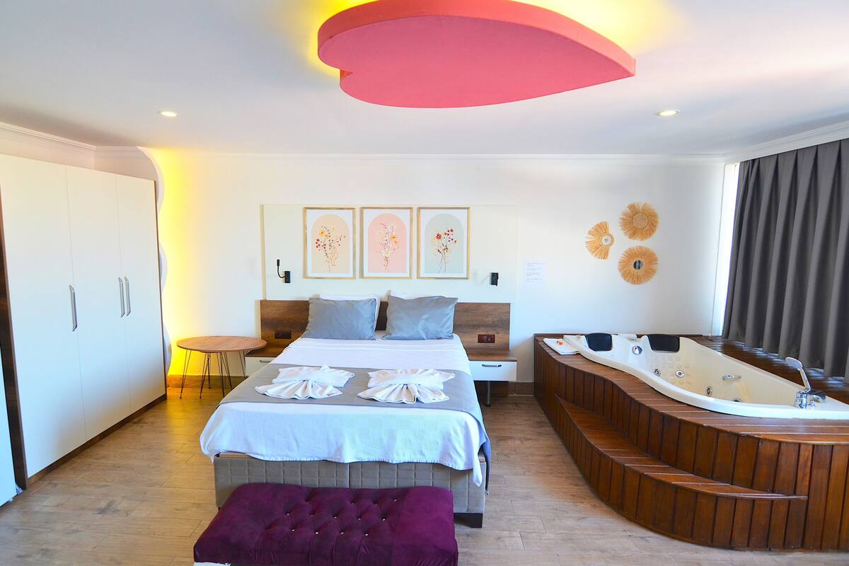 Habitación de hotel moderna con una cama grande, una bañera de madera y una mesita redonda.