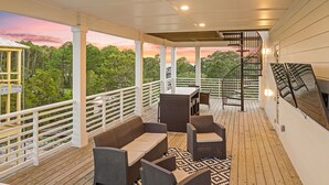 Una terraza techada al aire libre con asientos, una escalera y vistas a los árboles circundantes.