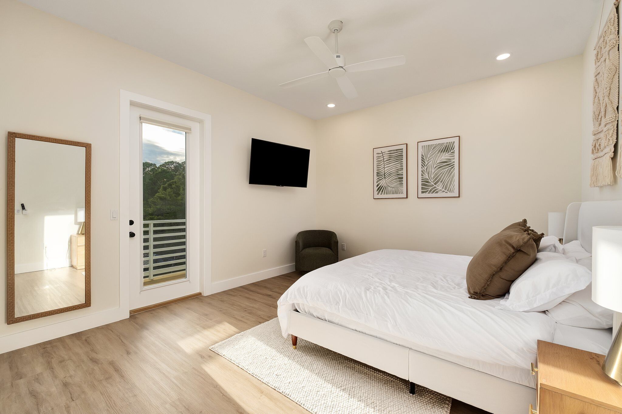 A bedroom with a bed, a ceiling fan, a TV, and artwork on the wall.