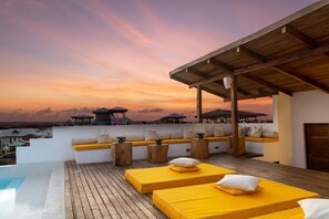 A rooftop terrace with wooden deck, yellow beds, and a view of the sunset over the ocean. - Upendo House Hotel (Zanzibar Town)