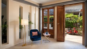 A room with a blue armchair, a floor lamp, and a small table with a glass. There is a wooden door leading outside. - Upendo House Hotel (Zanzibar Town)
