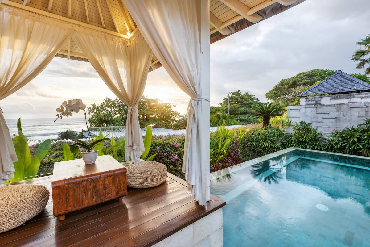 A wooden deck with a pool, surrounded by lush greenery and a view of the sea.