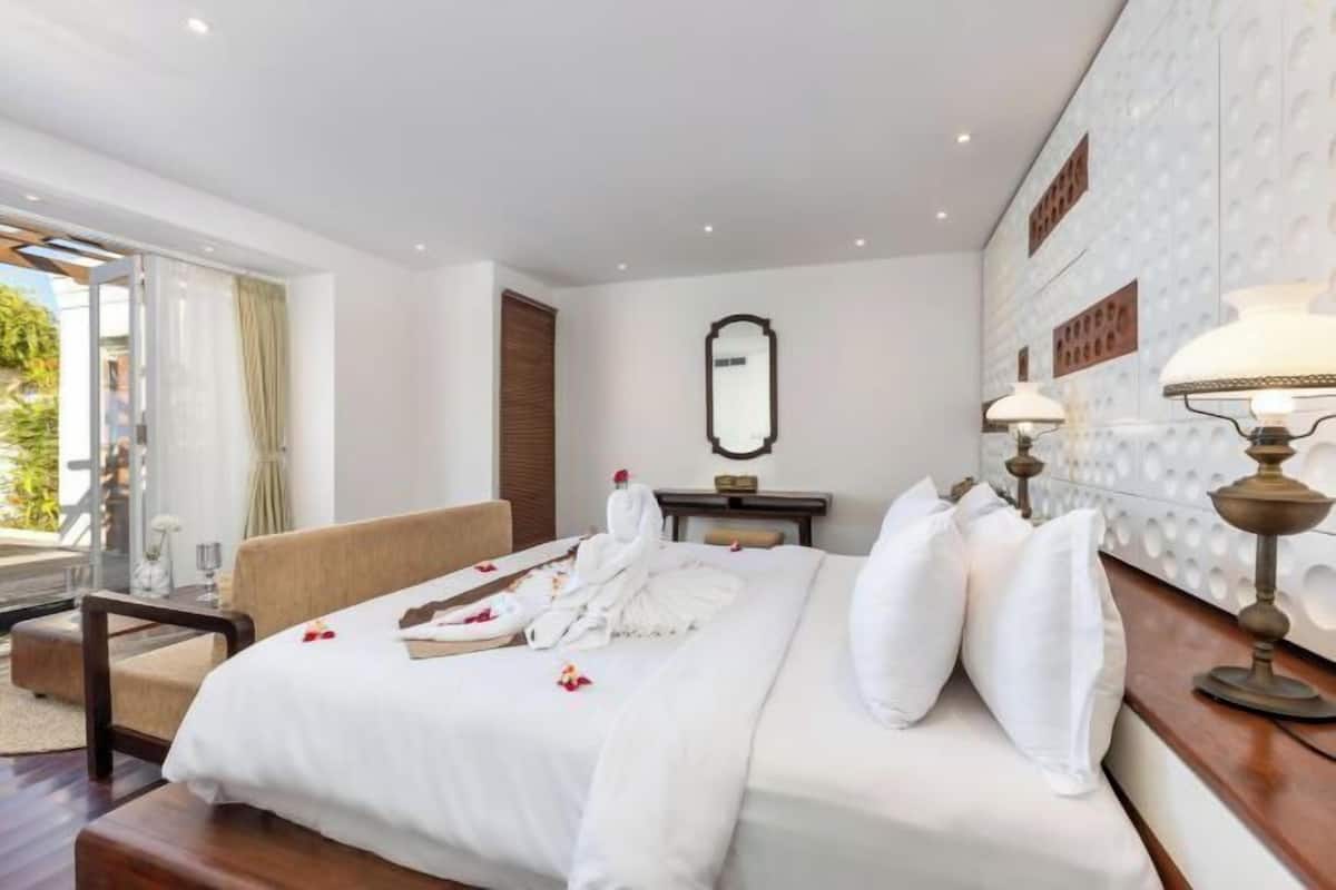 A hotel room with a large bed, a sofa, a desk, and a view of the outdoors.